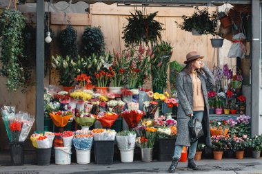 Genç ve güzel bir turist parlak buketler ve çiçeklerle dükkanın arka planına bakıyor.