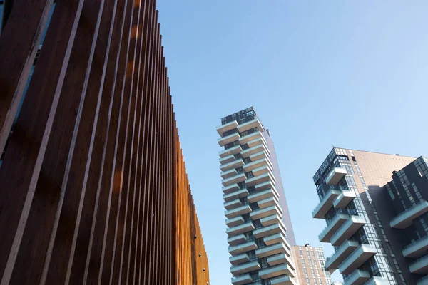 नीले आकाश के खिलाफ उच्च वृद्धि वाली इमारतों के साथ महानगर की पृष्ठभूमि के खिलाफ असामान्य लकड़ी की संरचना। 01.2020 मिलान — स्टॉक फ़ोटो, इमेज
