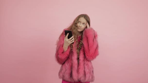 The young girl in a pink coat looked at the black mobile phone and thought. — Stock Video