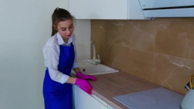 Güzel genç kız temizlik için pembe eldivenlere leke sürüyor. Mutfak dolaplarının eksiksiz temizlenmesi, dolabın yan yüzeyinin yıkanması.
