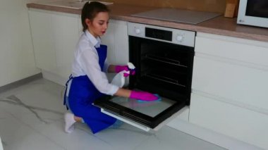Güzel genç bir kız fırını temizlemek için pembe eldivenlere deterjan ile siler..