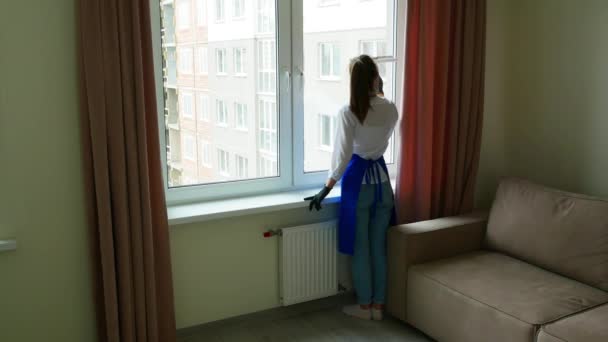 Schöne junge brünette Mädchen stehen mit dem Rücken und putzen. In vollem Wachstum. Das Mädchen wäscht ein Fenster mit einer speziellen Bürste zum Fensterputzen. — Stockvideo