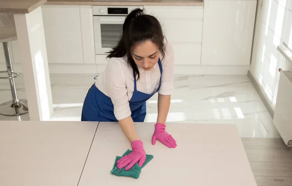 Uma menina limpa uma mesa com um pano azul de microfibra. Limpeza profissional . — Fotografia de Stock