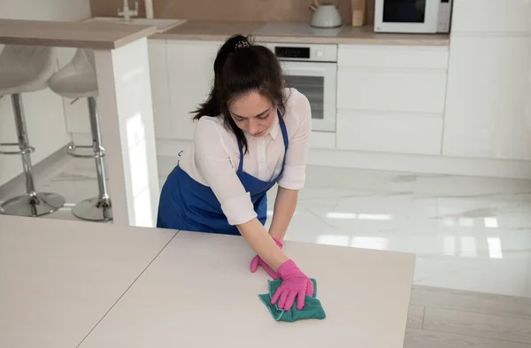 A menina faz uma limpeza completa na cozinha. Limpa uma superfície branca com um pano de microfibra . — Fotografia de Stock