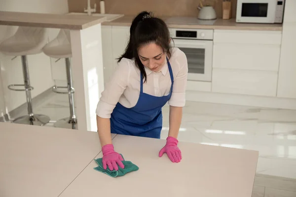 Menina bonita nova em luvas de borracha rosa esfrega a mesa com uma toalha. Limpeza profissional . — Fotografia de Stock