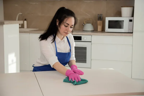 Menina morena bonita faz a limpeza na cozinha e limpa a superfície com pano de microfibra . — Fotografia de Stock