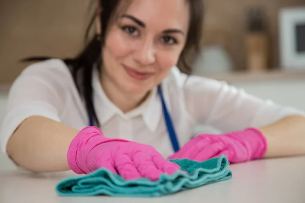 Közelkép egy barna lányról, aki takarítja a konyhát és mosolyogva néz a kamerába. Tisztítás örömmel. — Stock Fotó