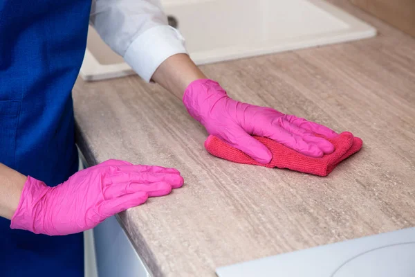 Pembe lastik eldivenli bir kız mikrofiber bezle ahşap bir yüzeyi yıkıyor..