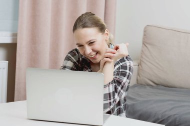 Evde pijamalarıyla oturan genç bir kız sosyal ağlarda iletişim kuruyor ve gülümsüyor..