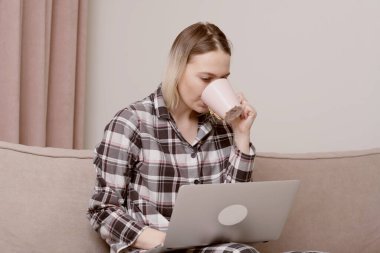 Kareli pijamalı genç bir kız dizüstü bilgisayarın önünde çalışıyor..