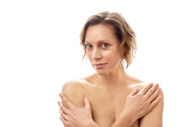 Kısa saçlı güzel genç bir kadın elleriyle kendine sarılıyor. Temiz cilt. Tepeden tırnağa çıplak poz. izole edilmiş beyaz arkaplan.