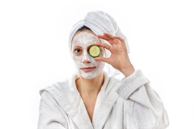 Beyaz kremalı yüzü ve sulu taze salatalıkları olan güzel genç bir kadın. Beyaz izole arkaplan.