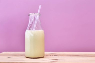 Pembe arka planı olan bir şişe sütün yakın çekimi..