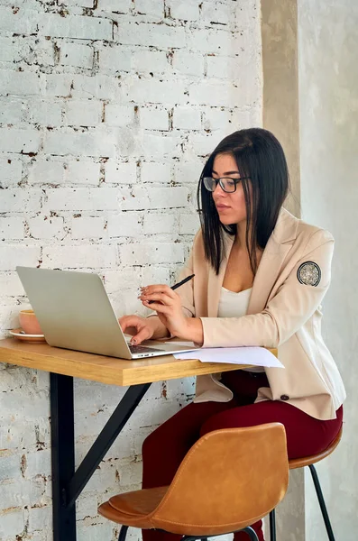 A black-rimmed freelancer girl works in a trendy cafe with a white laptop.