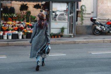 Genç ve güzel bir turist, parlak buketleri ve çiçekleri olan bir dükkanın arka planında karşıdan karşıya geçiyor..