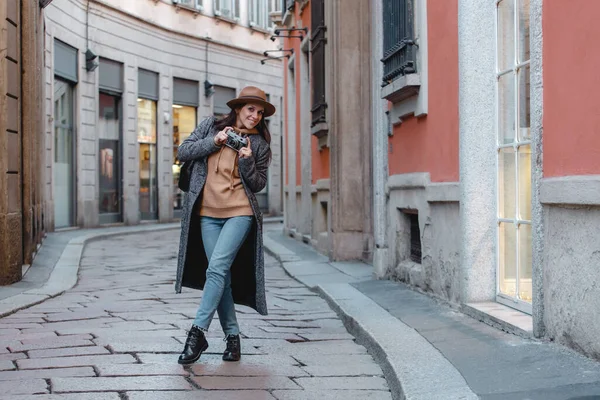 Девушка-туристка с камерой в руках улыбается на фоне маленькой старой улицы в оранжевых тонах . — стоковое фото