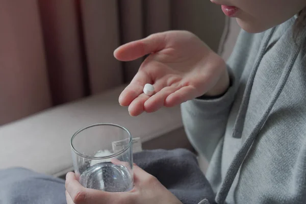 woman takes pill in one hand and glass of water in another