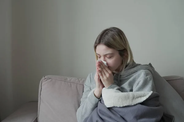 Mujer enferma sentada en el sofá y estornudando en el tejido — Foto de Stock