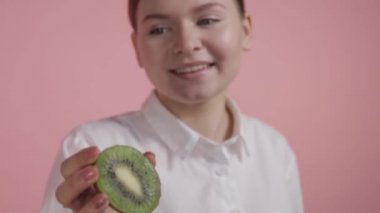 Doğal güzelliği olan genç bir kız olgun parlak bir kiviyi elinde tutuyor ve kameraya bakıyor..