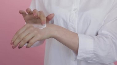 Pembe arka planda nemlendiricinin kadın ellerine sürtünmesi.