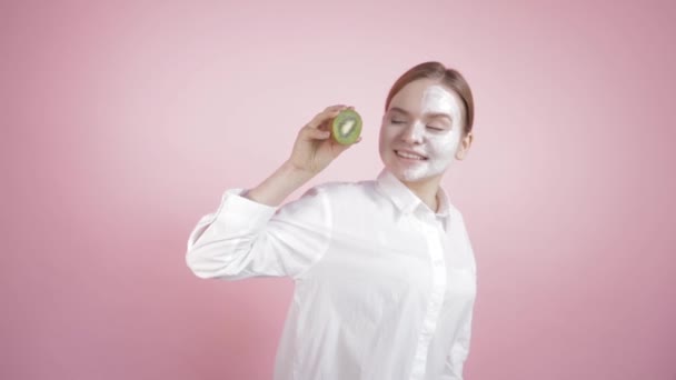 一半的脸贴在一个拿着成熟的猕猴桃的小女孩的奶油里. — 图库视频影像