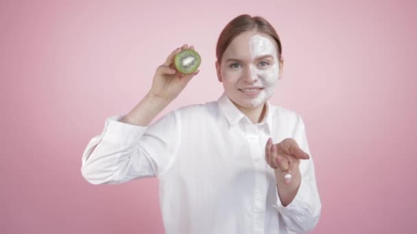 Metà del viso nella crema di una giovane ragazza che mostra che la sua crema è naturale come questo kiwi . — Video Stock