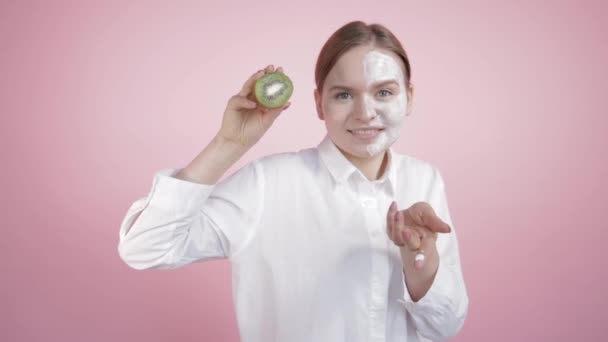 Die Hälfte des Gesichts in der Creme eines jungen Mädchens, das zeigt, dass ihre Creme so natürlich ist wie diese Kiwi. — Stockvideo