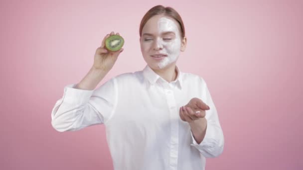 Het meisje toont op haar hand een gezichtscrème, en in de andere hand sappige kiwi. — Stockvideo