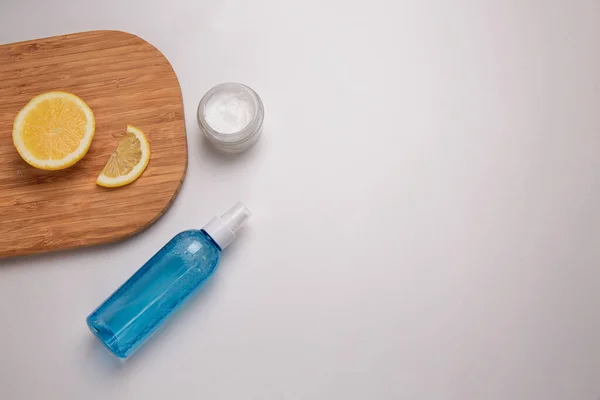 A jar of white moisturizer. Wooden Board with a slice of lemon. The concept of natural cosmetics. Micellar water in the blue jar. — Stock Photo, Image