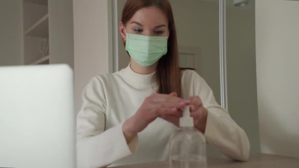 Όμορφη νεαρή κοπέλα σε μια ιατρική μάσκα αντιμετωπίζει τα χέρια με αντισηπτικό στο σπίτι. Orvi, coronovirus, οξεία αναπνευστική νόσο. — Αρχείο Βίντεο