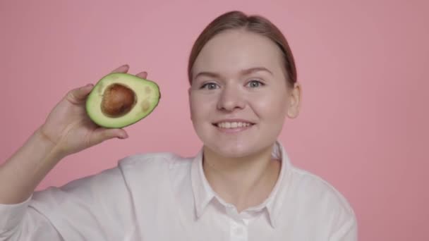 Ripe avocado in the hands of a young girl on a pink background. — Stock Video