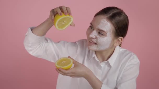 Chica alegre sosteniendo dos limones en sus manos, crema blanca en su cara . — Vídeo de stock