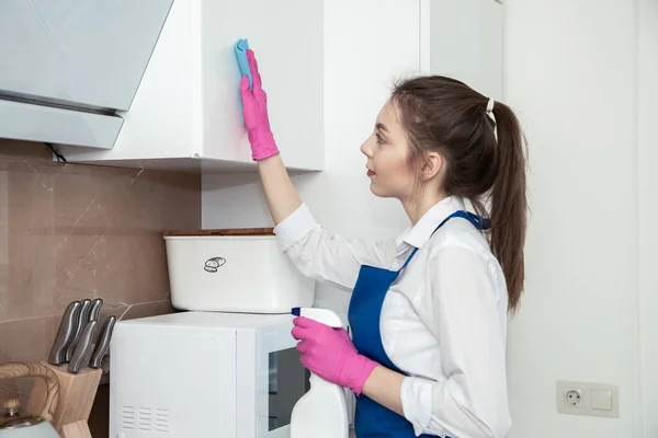 Brünette mädchen putzt die küche. Reinigt die Oberfläche eines glänzend weißen Gehäuses. Reinigung der Küche. — Stockfoto