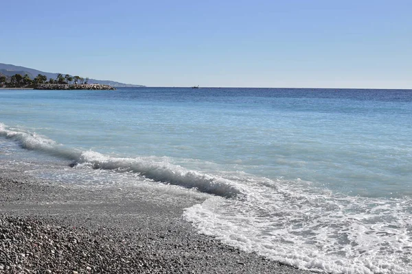 Praia pedregosa com pequenas pedras redondas. Uma onda do mar . — Fotografia de Stock