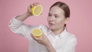 Genç bir kız iki büyük limon dilimini elinde tutuyor ve limon suyunu sıkıyor..