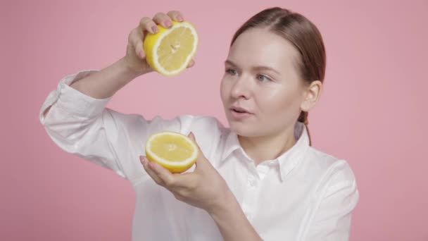 Une jeune fille tient deux grandes tranches jaunes de citron dans ses mains et presse le jus d'un citron . — Video