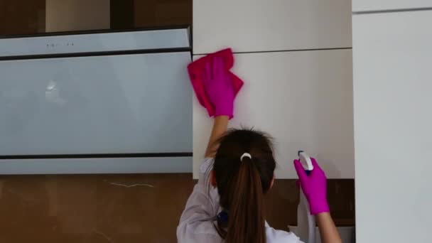 Seorang gadis berambut cokelat berdiri di punggungnya dan melakukan pembersihan. Menggosok permukaan putih. Sarung tangan merah muda untuk membersihkan. — Stok Video