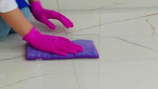 Девушка стоит на коленях и вытирает пол обеими руками с фиолетовой тряпкой в розовых перчатках. . — стоковое видео