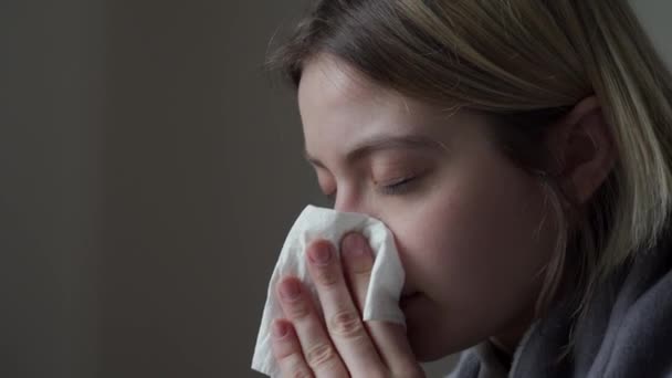 La rubia se sienta con los ojos cerrados, tiene enfermedades virales y se sopla la nariz. Síntoma de Orvi, coronovirus, gripe, alergia — Vídeos de Stock
