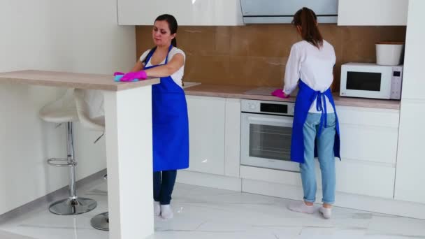 Duas lindas garotas atraentes terminam de limpar em uma cozinha branca e brilhante e saem. Limpeza profissional . — Vídeo de Stock