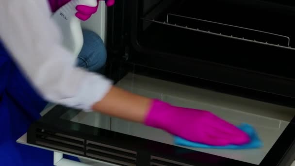 Primer plano de una hermosa niña limpia el horno con un detergente en guantes de color rosa para la limpieza. Vista lateral . — Vídeo de stock