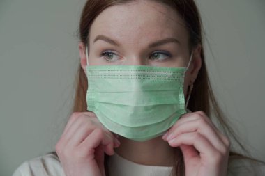 Tıbbi maske takan uzun kızıl saçlı güzel bir genç kıza yaklaş. Orvi, koronovirüs, grip, akut solunum enfeksiyonları..