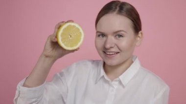 Pembe arka planda gülümseyen genç bir kızın ellerinde olgun bir limon..