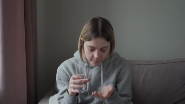 Una niña enferma, cansada de los medicamentos, toma una pastilla y la bebe con agua con un vaso transparente . — Vídeo de stock