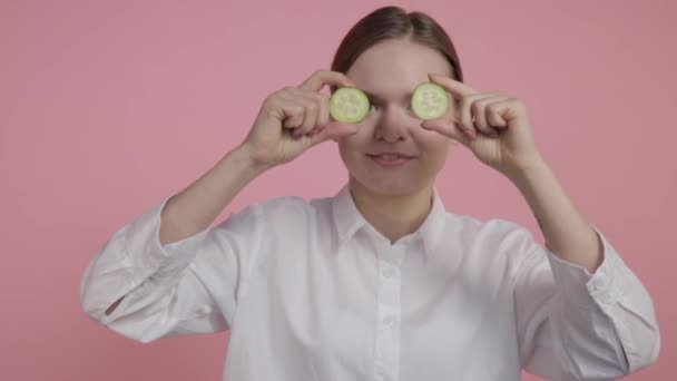 Egy fiatal lány smink nélkül két szelet uborkát tart a szeme előtt.. — Stock videók
