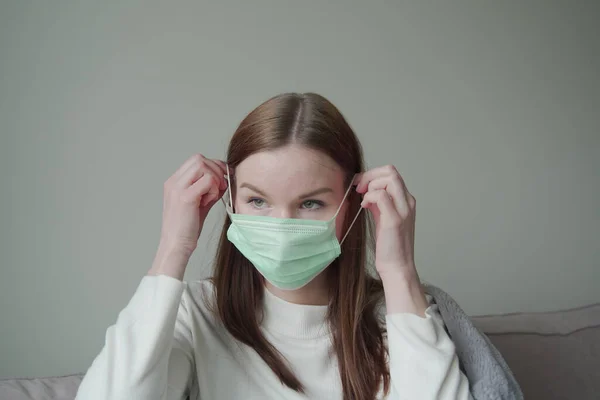 白いブラウスと赤い髪の美しい若い女の子は彼女の顔に緑の医療マスクを置きます。Orvi,コロノウイルス,インフルエンザ,急性呼吸器感染症. — ストック写真