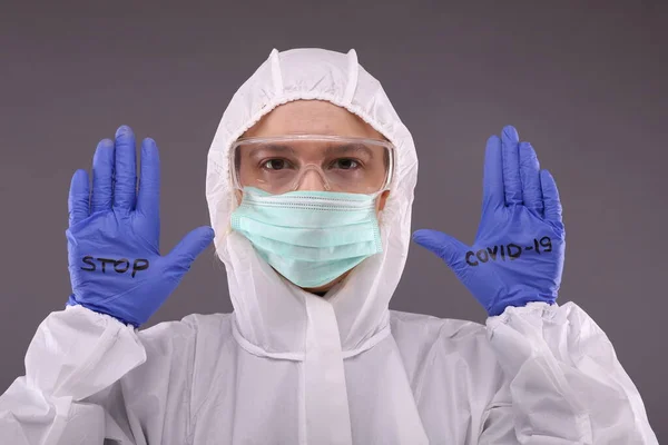 Vrouw in beschermend kostuum en blauwe handschoenen met bordje "stop COVID-19" — Stockfoto