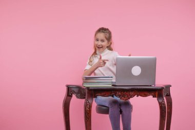 Çerçeveye bak. Beyaz gömlekli ve kot pantolonlu genç bir kız dizüstü bilgisayar ekranını işaret ediyor ve gülümsüyor..