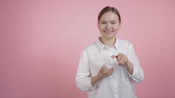 En ung flicka med naturlig skönhet öppnar en burk vit grädde — Stockvideo