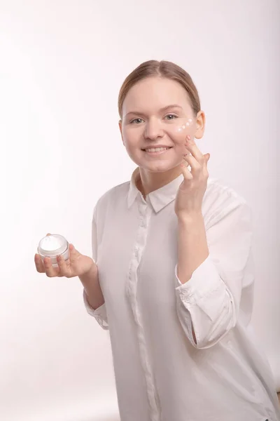 Meisje houdt een handcrème vast. Het meisje veroorzaakt in het gezicht van natuurlijke gezichtscrème. — Stockfoto